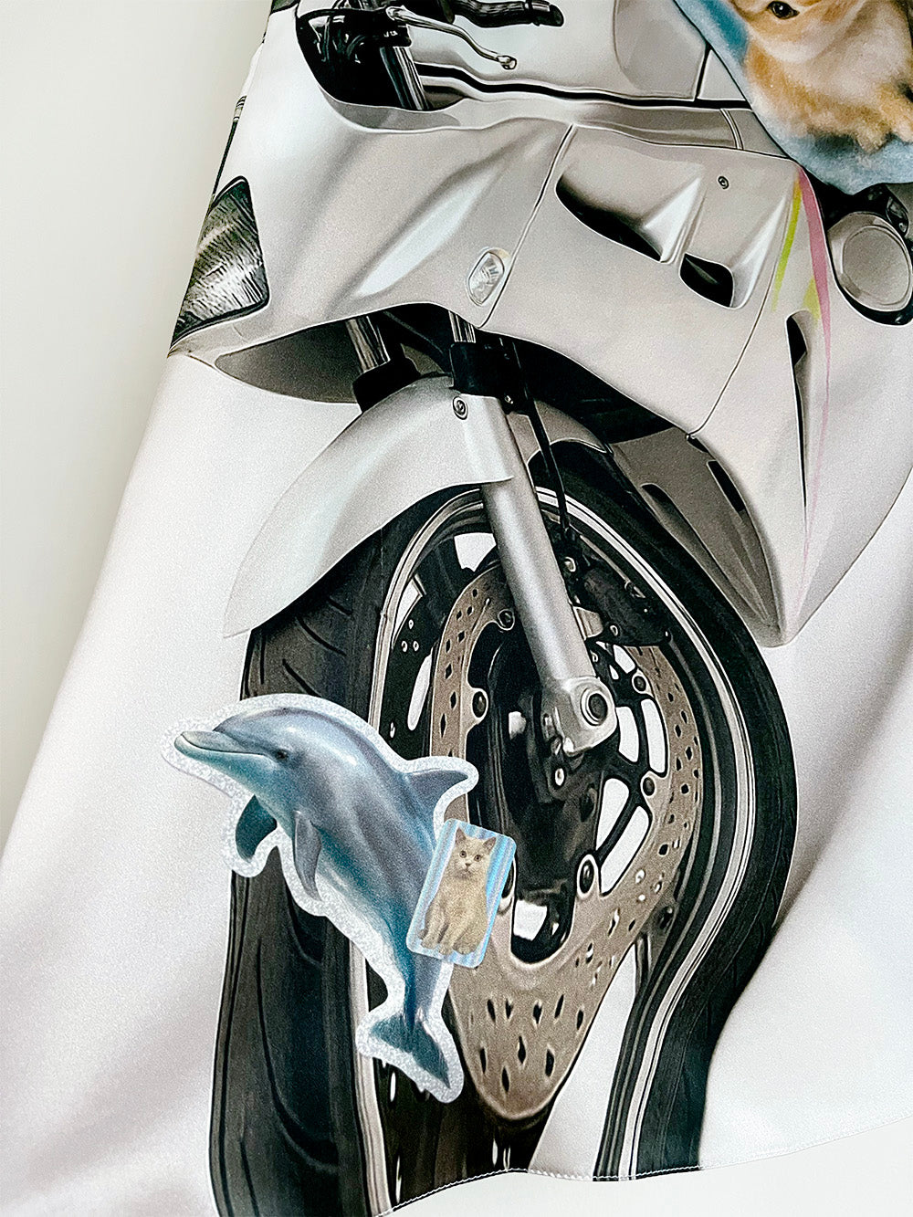 Close-up of a white motorcycle with a dolphin and cat sticker on the wheel print.
