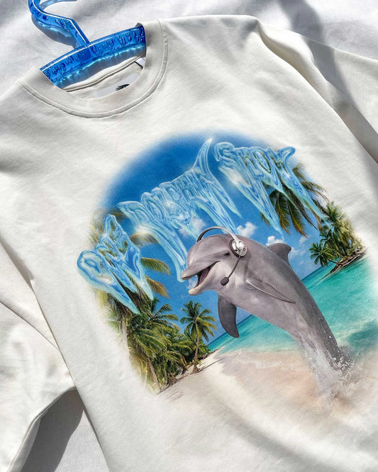 Close-up of the One Dolphin Show T-shirt by Chimera Lab, featuring a vibrant beachcore digital print with a dolphin in a headset jumping from turquoise water, shot in natural sunlight on a blue plastic Y2K-style hanger.