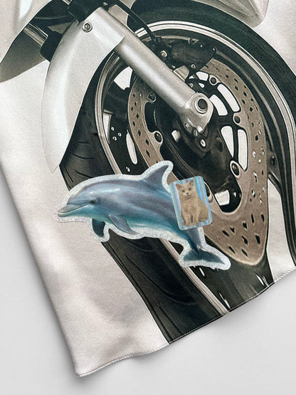 Close-up of a motorcycle wheel with a dolphin and cat sticker print on a white background.