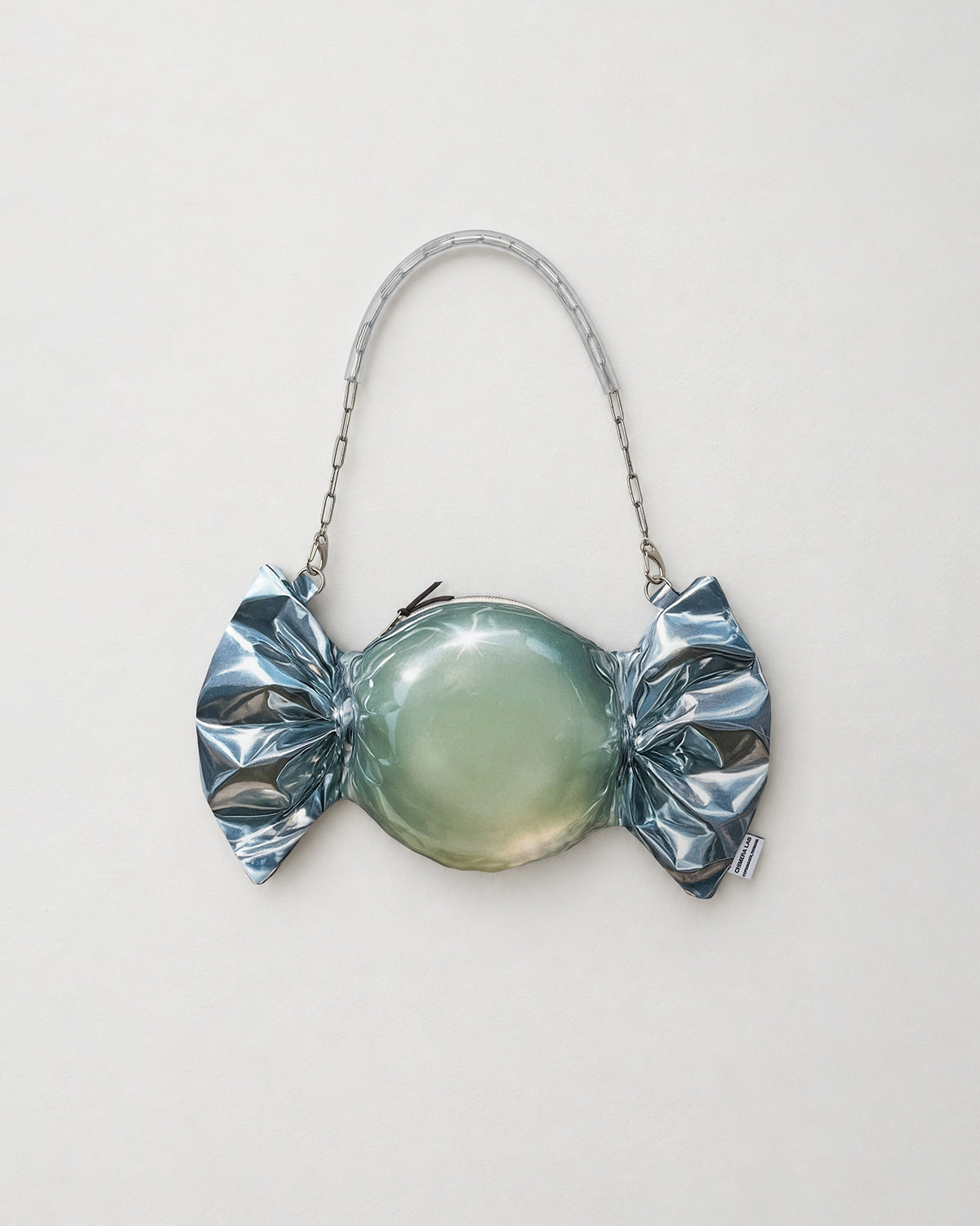 A novelty candy-shaped clutch purse with a metallic silver foil-wrapped print body, a glossy pale green center, and a silver chain handle, shown on a plain light gray background.