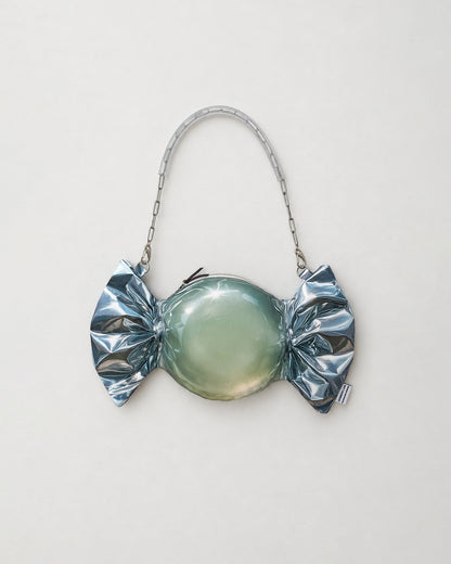 A novelty candy-shaped clutch purse with a metallic silver foil-wrapped print body, a glossy pale green center, and a silver chain handle, shown on a plain light gray background.