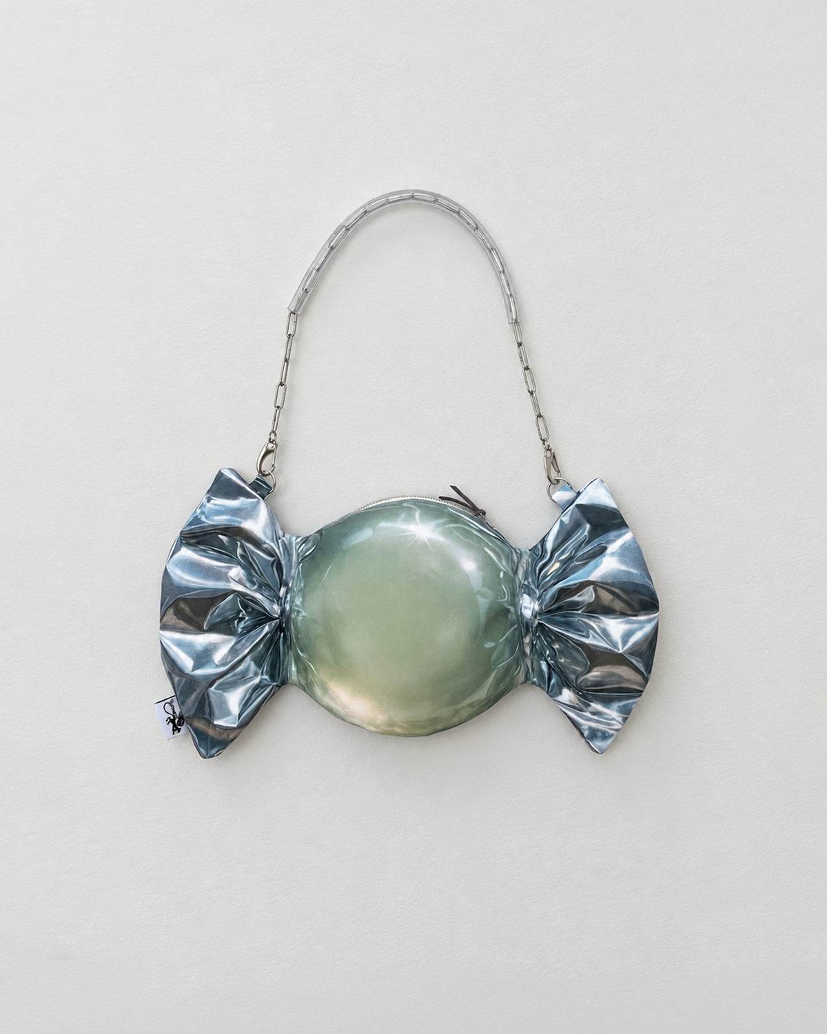 A novelty candy-shaped purse or clutch with a metallic silver foil-wrapped print, a smooth oval center, and a silver chain handle, shown against a plain light background.