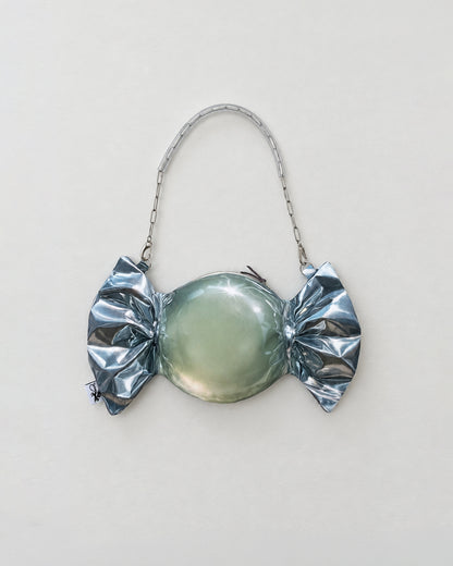 A novelty candy-shaped purse or clutch with a metallic silver foil-wrapped print, a smooth oval center, and a silver chain handle, shown against a plain light background.