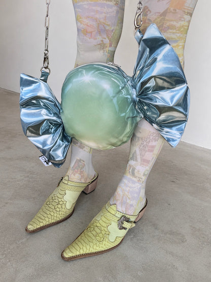 Person wearing a candy-shaped bag in a silver metallic wrap print and pointed shoes on a plain background