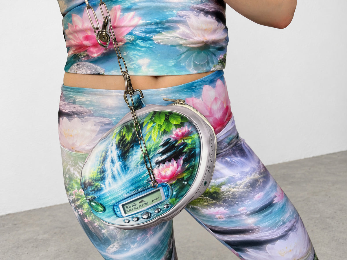 A person wears a matching printed two-piece outfit with a floral and landscape design and holds a round printed bag with a chain strap. The bag features a scenic print of a waterfall and pink lotus flowers.
