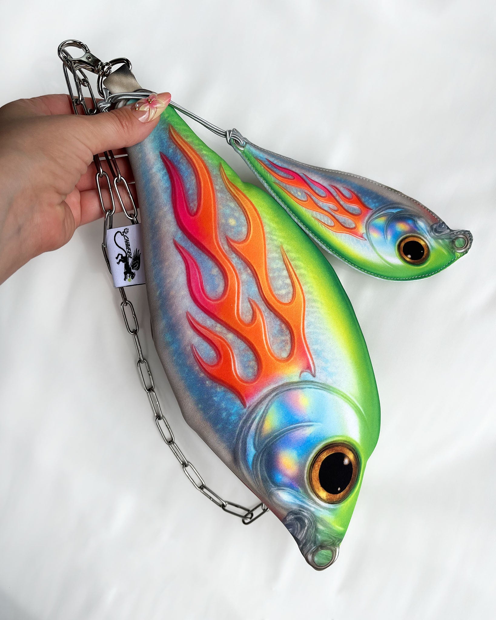 Hand holding Baby Trophy Fish pouch with holographic finish, flame design, and stainless steel chain strap.