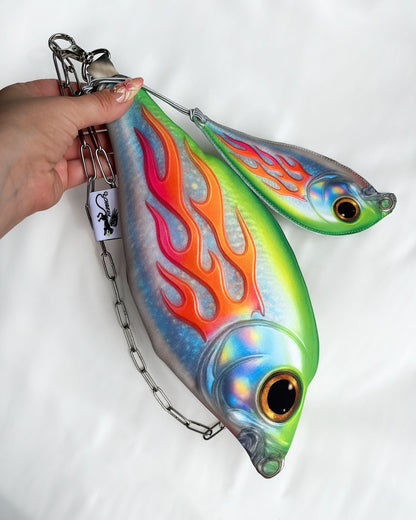 Hand holding Baby Trophy Fish pouch with holographic finish, flame design, and stainless steel chain strap.