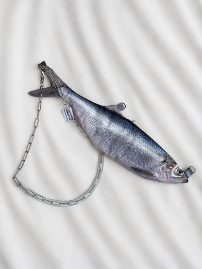 A fish-shaped clutch bag with a silver chain strap, displayed on a white textured fabric background.