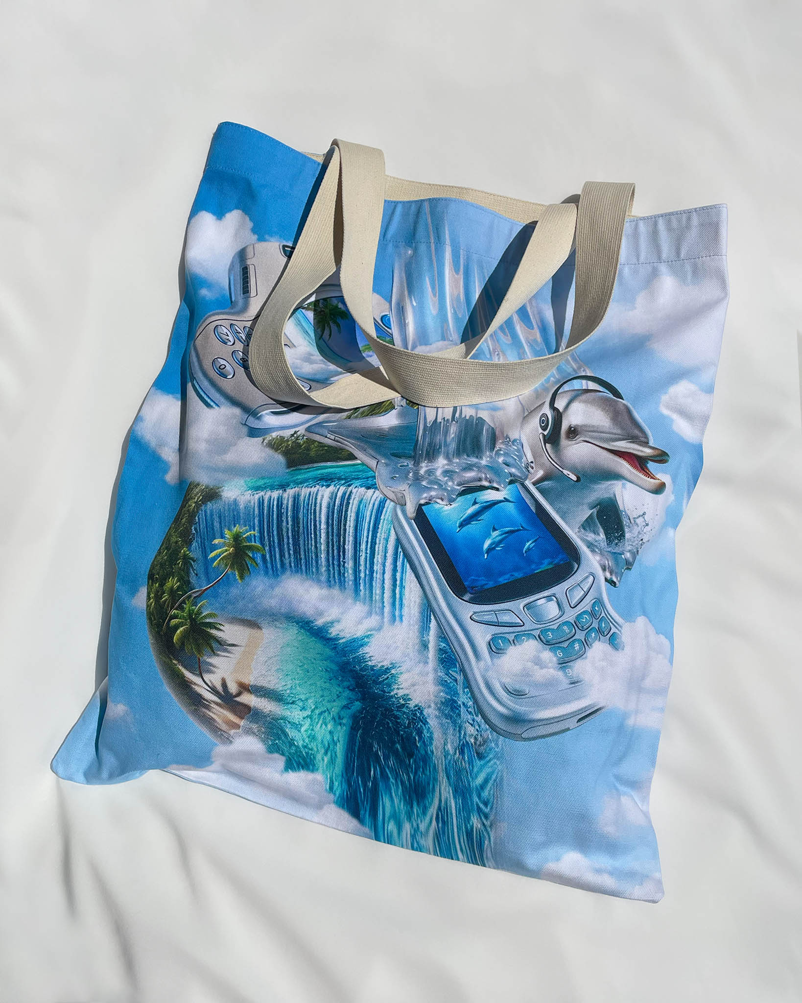 Flat lay of the Dreamline OS Large Cotton Canvas Tote Bag by Chimera Lab on white background, showcasing full surreal print with tropical waterfalls, dolphins, and y2k phones.