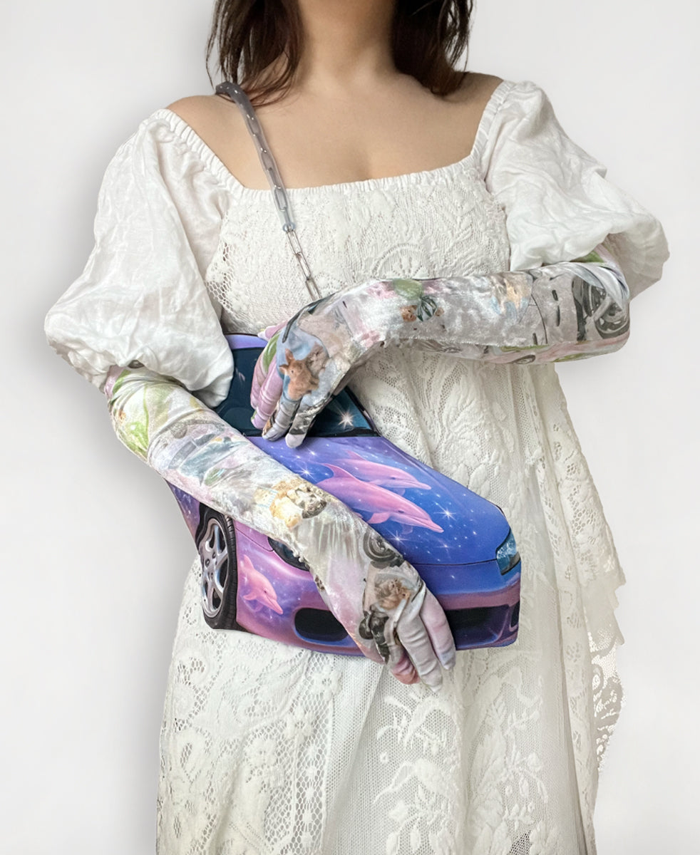 Person wearing a white lace dress with long printed opera gloves, holding a purple car print bag.