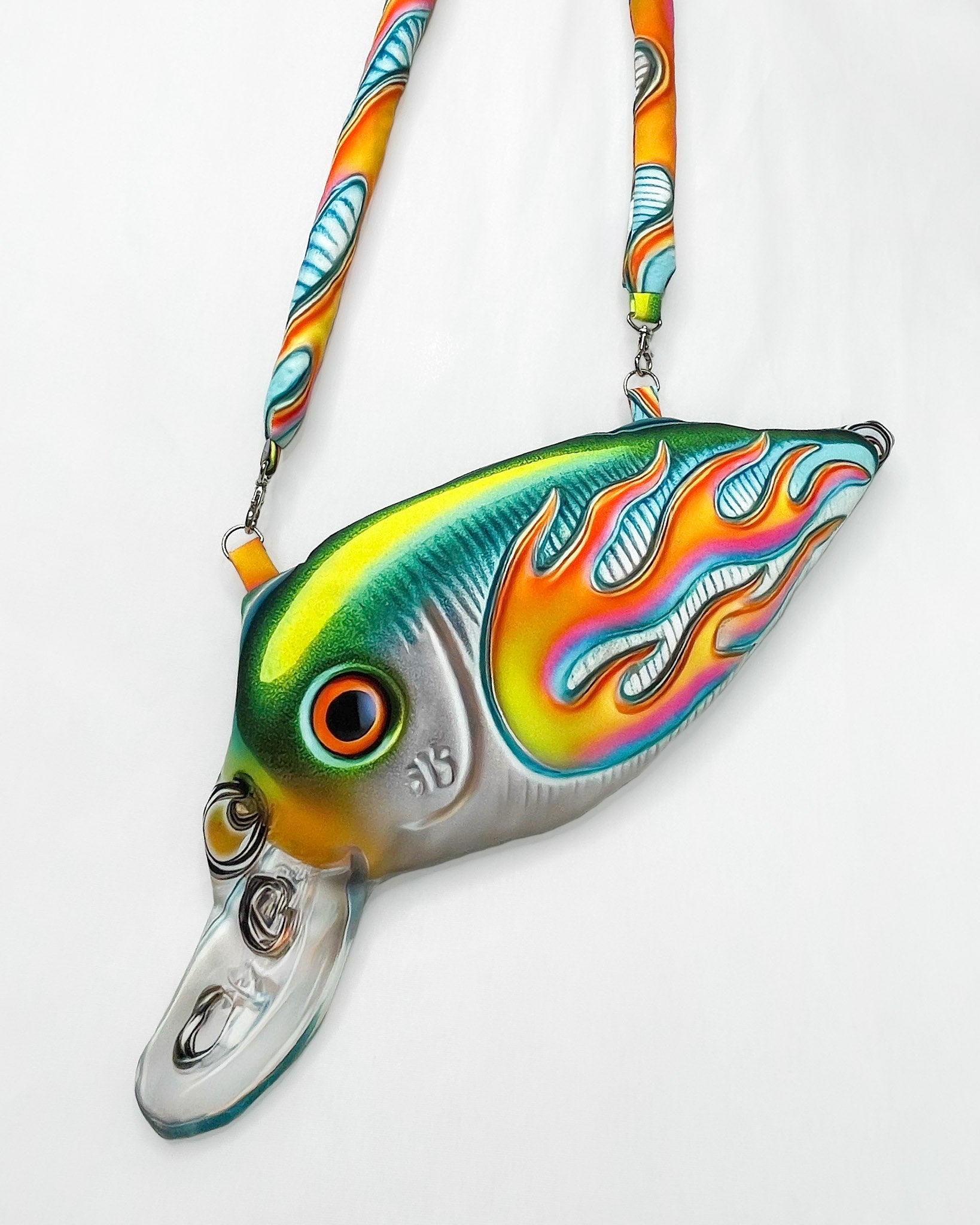 Close-up of the Moto Fish Bag by Chimera Lab, shaped like a 3D fishing lure with a chrome body and neon flame graphic, featuring a padded printed strap.