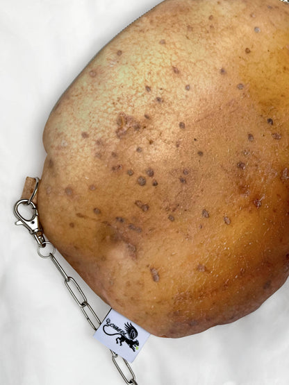 A close-up of a potato print accessory with a silver metal clasp and chain attached, resting on a white fabric background.