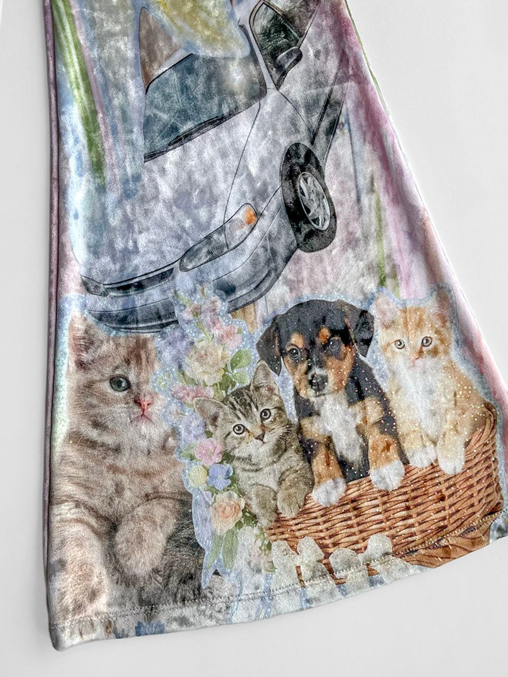 Fabric close-up with a design of cats and a dog in a basket, with a car in the background.