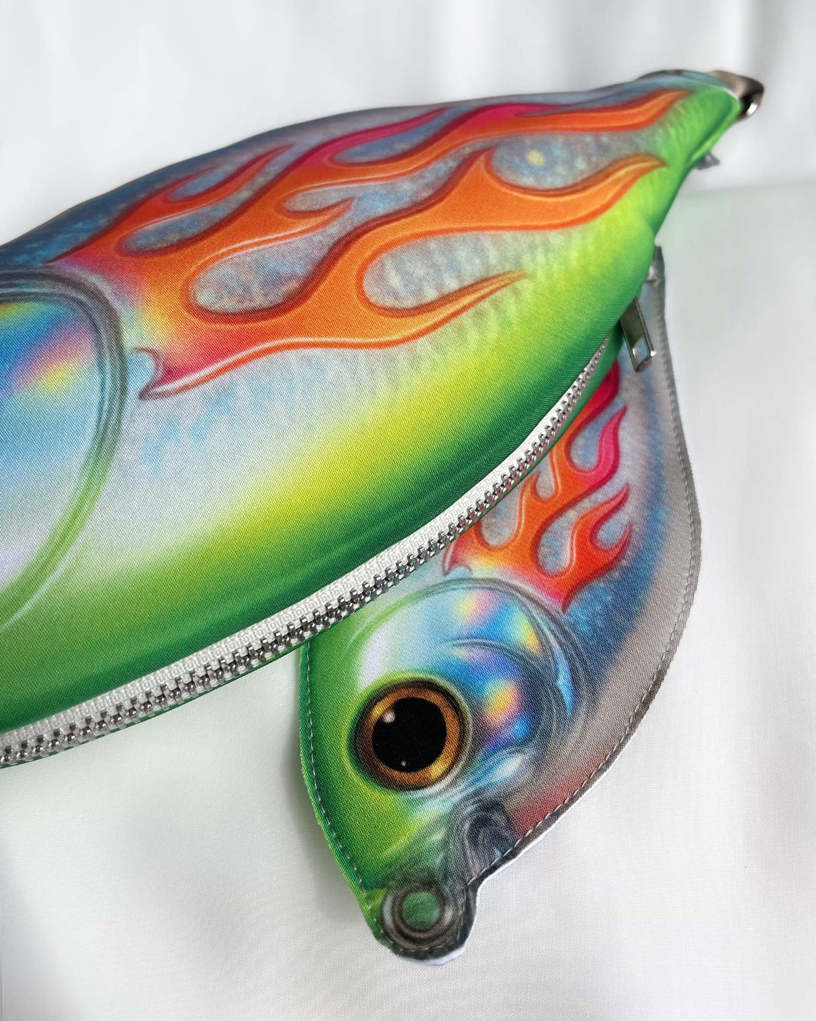Close-up of Baby Trophy Fish pouch showing holographic fish eye and neon flame print on softshell fabric.
