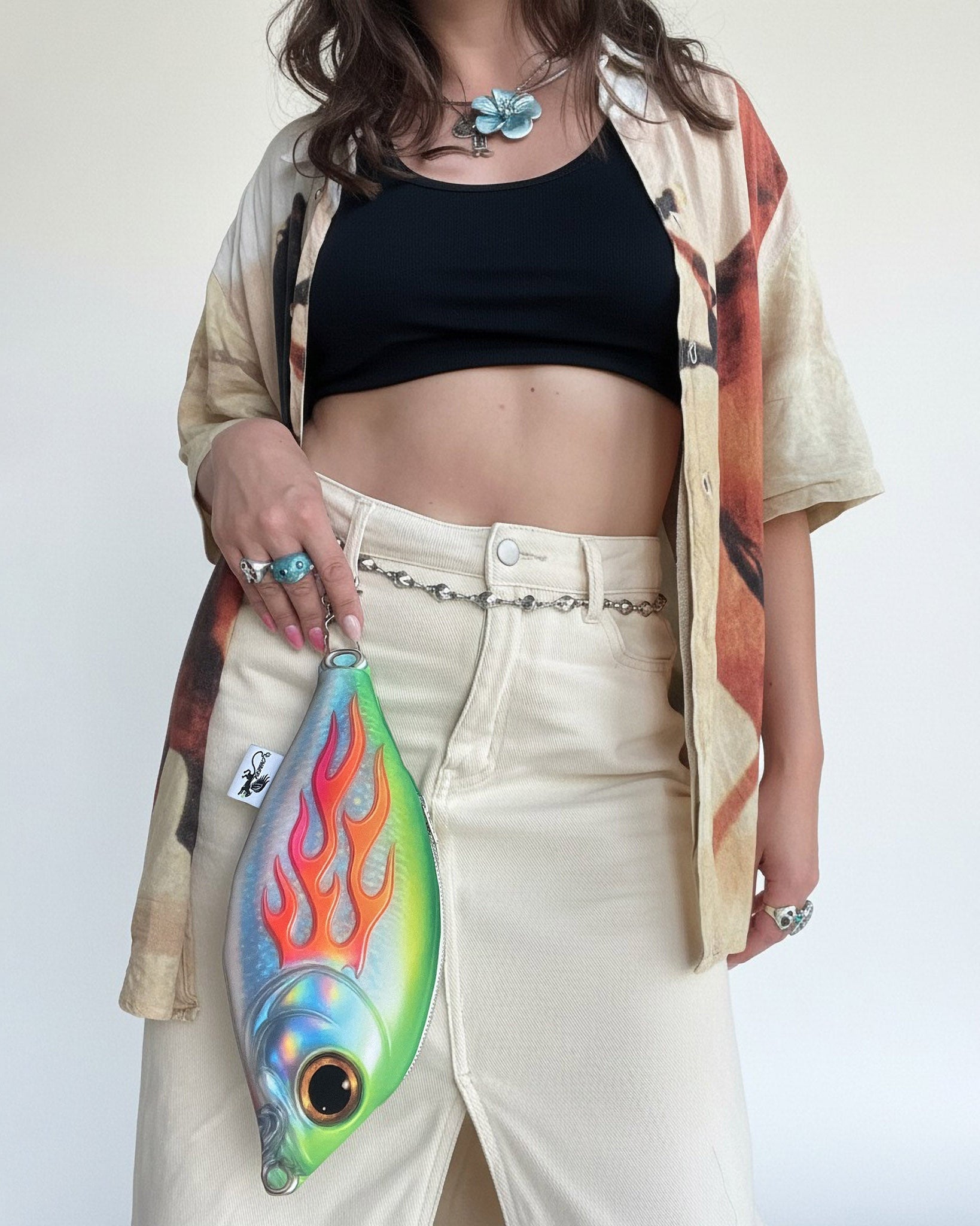 Model holding Baby Trophy Fish pouch with holographic flame print, worn as a surreal mini fish-shaped bag charm.